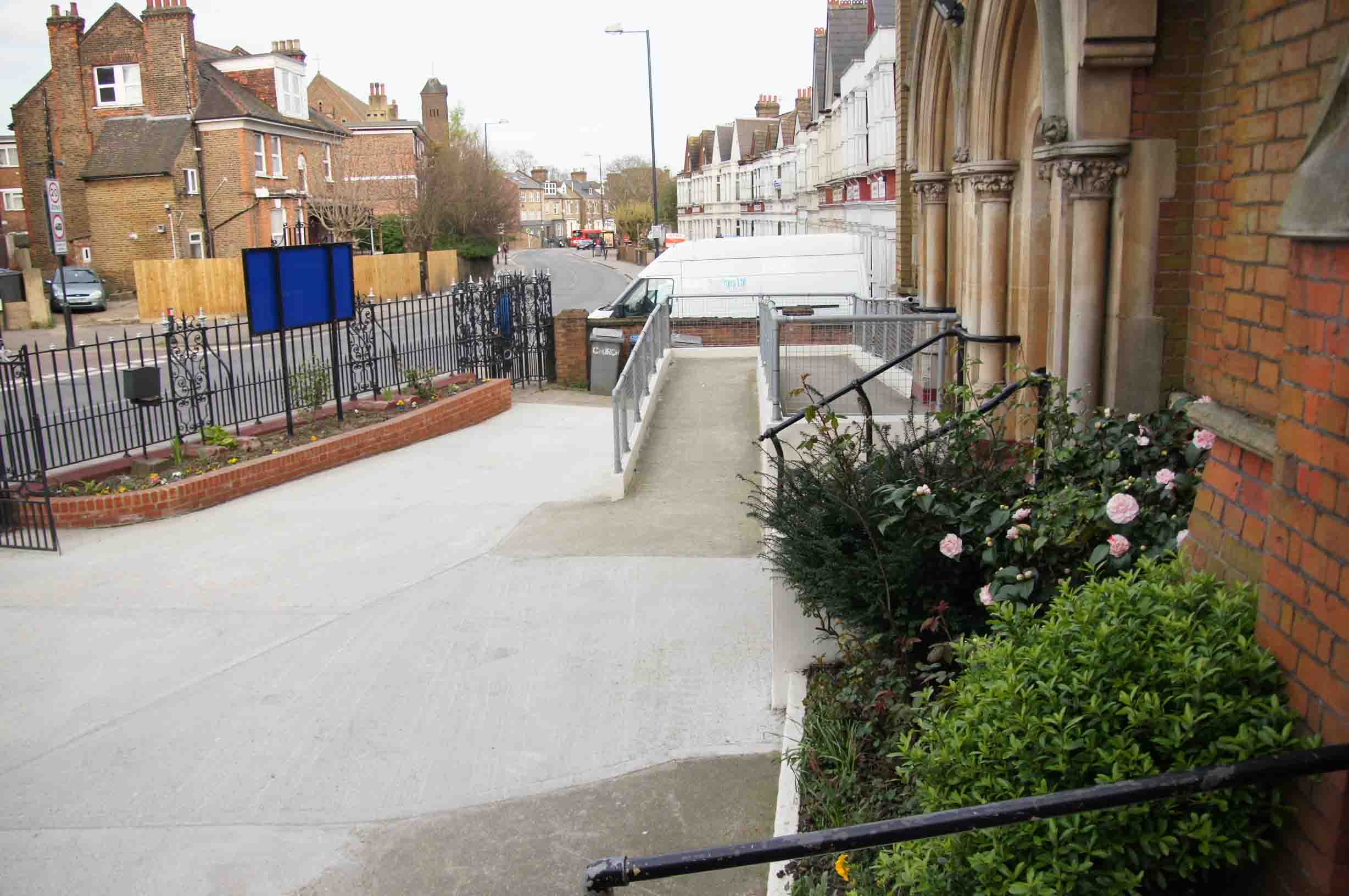 The accessibility ramp leading up to the main entrance of Harlesden Baptist Church on Acton Lane, with handrails on both sides and a gentle gradient suitable for wheelchairs and buggies