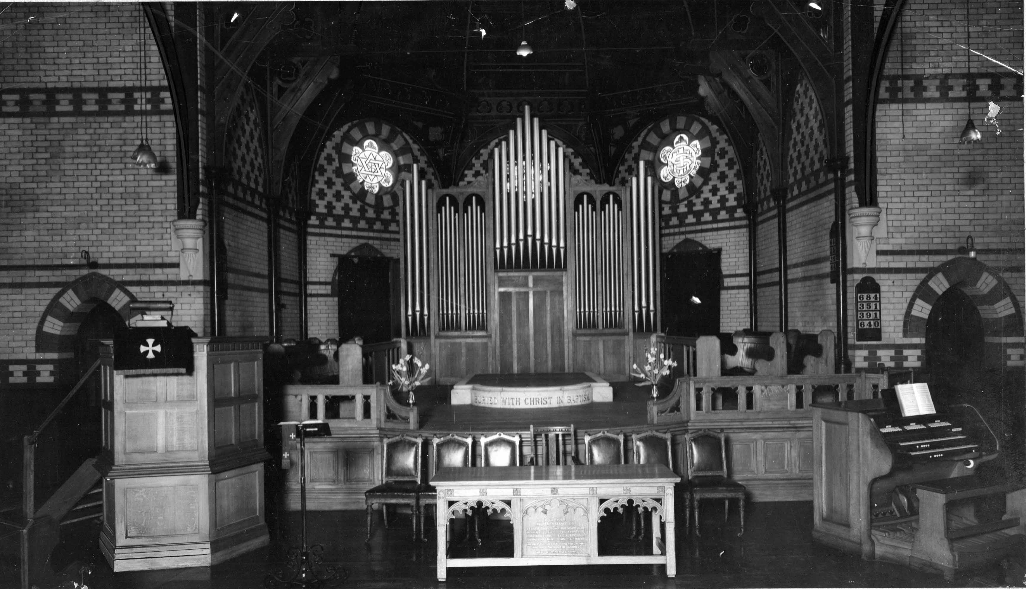 The front of Harlesden Baptist Church as it was in the early days, showing the pipe organ, the central cross, the wooden pulpit, the deacons' chairs and the original baptism pool at the foot of the platform